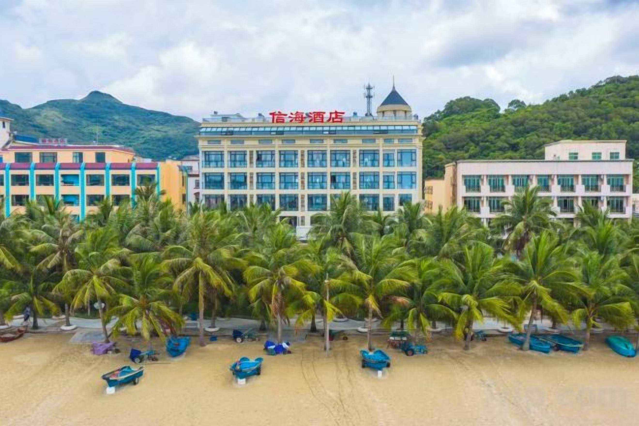 A hotel with a prominent building in the center, surrounded by palm trees and a sandy beach.