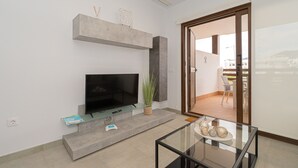Ein modernes Wohnzimmer mit Flachbildfernseher, Glastisch und einer Schiebetür zum Außenbereich.