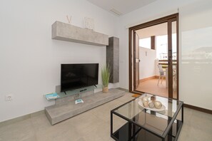 A modern living room with a flat-screen TV, a glass coffee table, and a sliding glass door leading to an outdoor area. - Apartamento Narcisos (Mar de Pupi) (San Juan de los terreros)