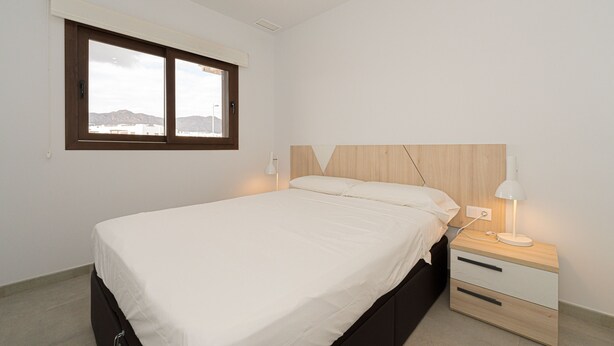 Ein Schlafzimmer mit Bett, Nachttisch mit Lampe, Fenster und Bergblick.
