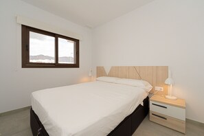 A bedroom with a bed, a nightstand with a lamp, a window, and a view of mountains.