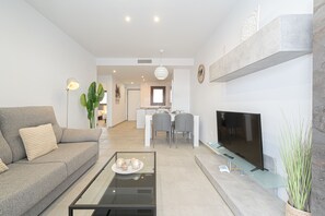 A modern living room with a sofa, coffee table, TV, and a dining area in the background. - Apartamento Narcisos (Mar de Pupi) (San Juan de los terreros)