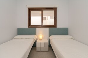 A small, clean room with two single beds, a nightstand with a lamp, and a window above the beds. - Apartamento Narcisos (Mar de Pupi) (San Juan de los terreros)