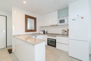 A modern kitchen with white cabinets, a granite countertop, a built-in microwave, and a refrigerator. - Apartamento Narcisos (Mar de Pupi) (San Juan de los terreros)