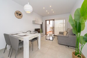 A modern living room with a grey sofa, a dining table with chairs, a large potted plant, and a world map on the wall. - Apartamento Narcisos (Mar de Pupi) (San Juan de los terreros)
