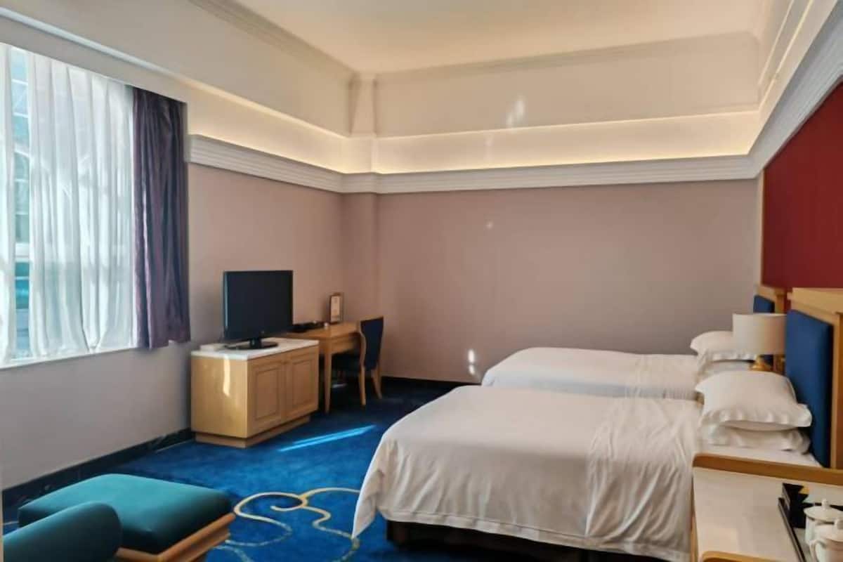A hotel room with two beds, a desk, a television, and a window with curtains.