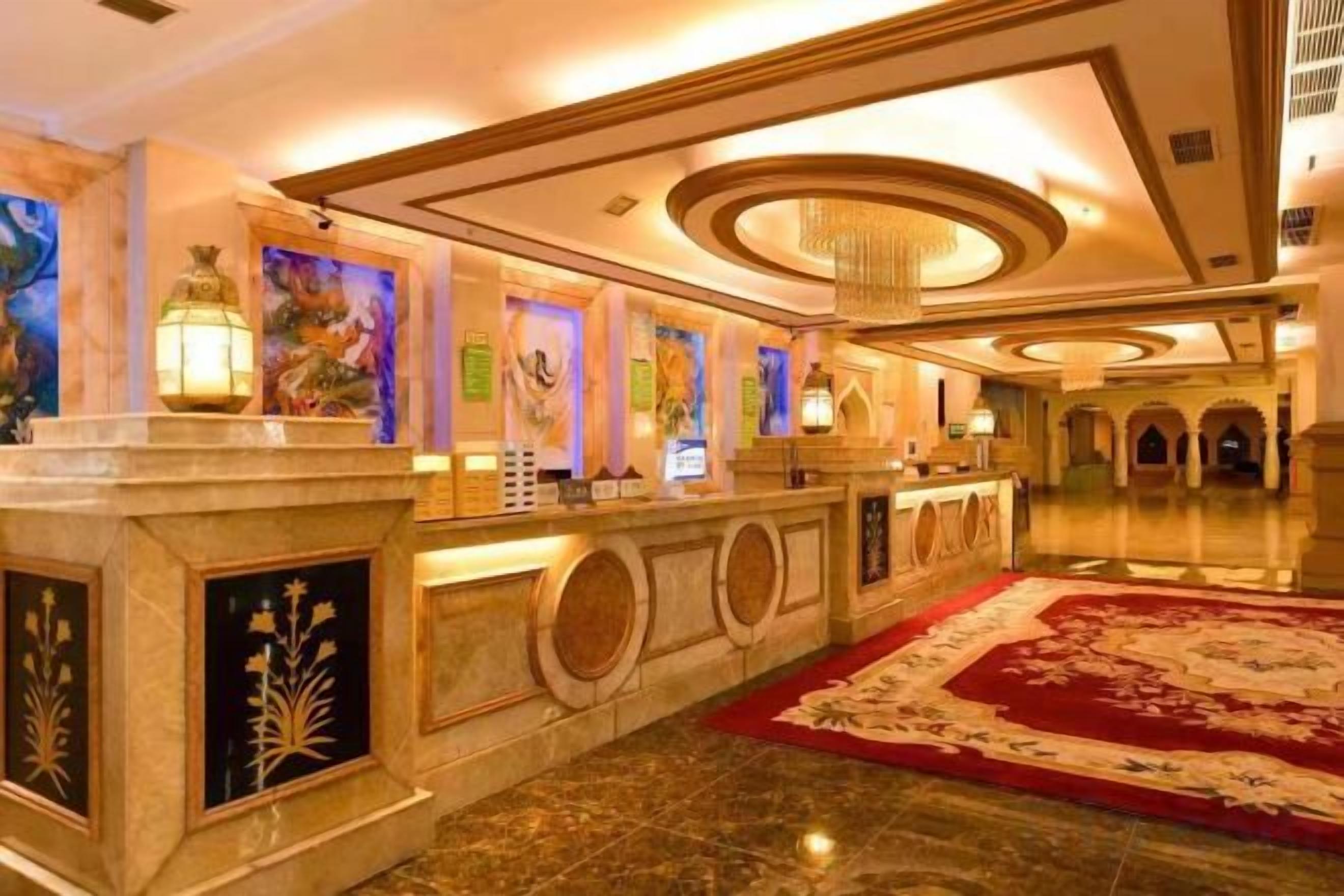 A hotel lobby with a reception desk, a red carpet, and a chandelier.