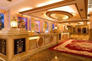 A hotel lobby with a reception desk, a red carpet, and a chandelier.