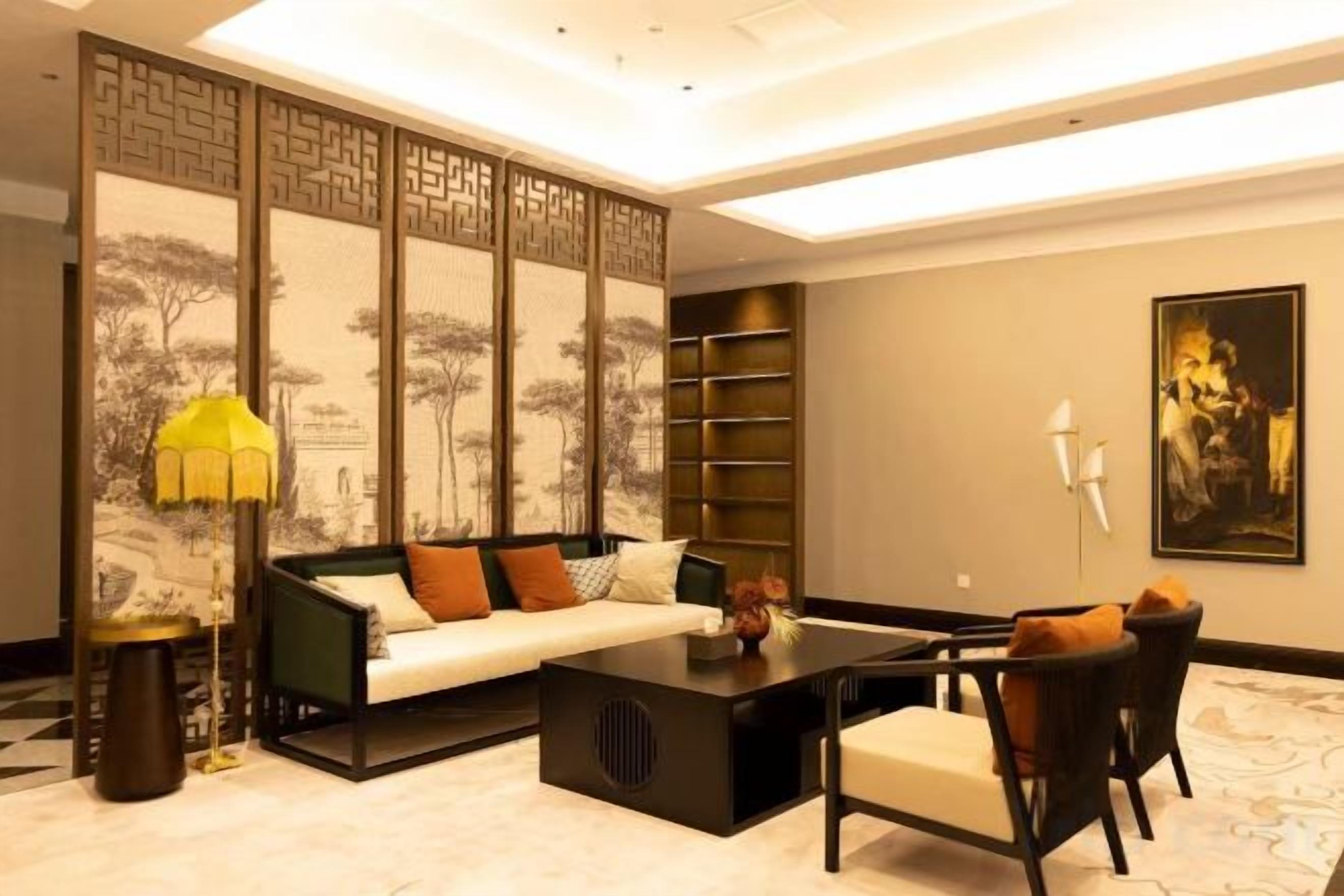A modern living room with a sofa, coffee table, and chairs, a decorative lamp, and a traditional screen with artwork.