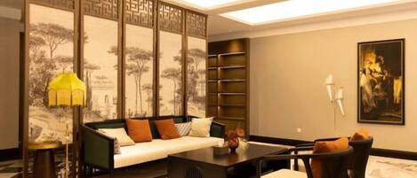 A modern living room with a sofa, coffee table, and chairs, a decorative lamp, and a traditional screen with artwork.