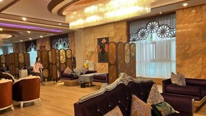A lobby with a reception desk, seating area with sofas and armchairs, decorative wall panels, and a chandelier. - Sun City Huiyue Hotel (Daying)