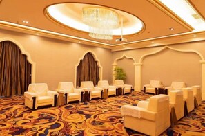 Un salón de conferencias con alfombra estampada, filas de sillas y una araña.