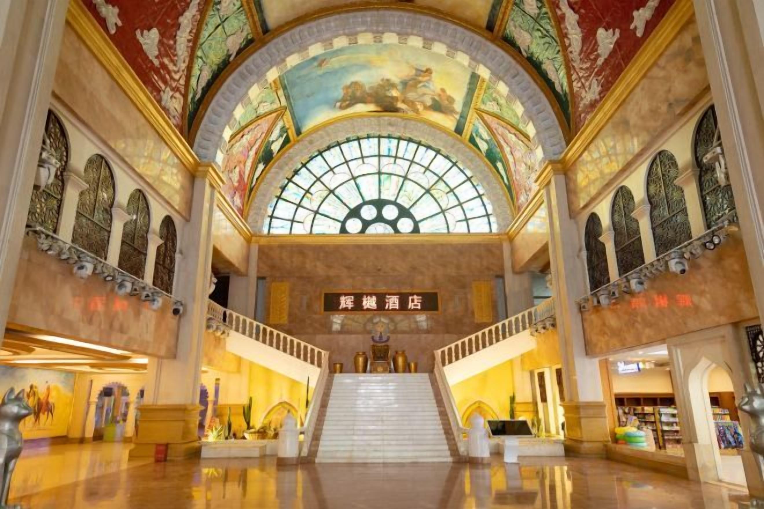 A grand interior with a central staircase, arched windows, and a large mural on the ceiling.