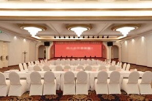 A conference room with round tables and white chairs, a stage with a red backdrop, and a carpeted floor.