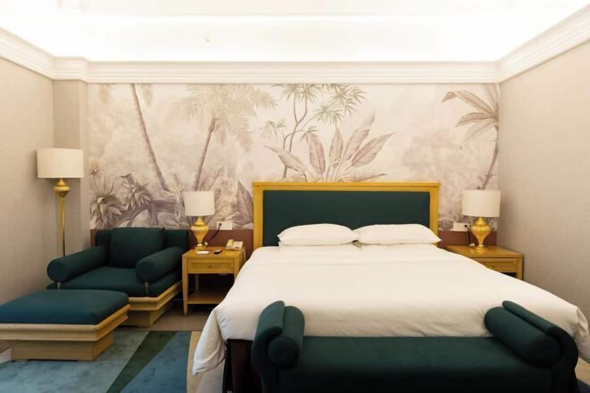 A hotel room with a bed, two bedside tables, a sofa, and a lamp.