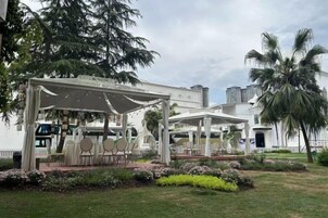 A covered outdoor seating area with tables and chairs, surrounded by landscaped gardens and palm trees.