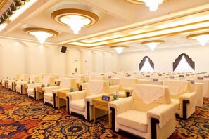 Un salón de conferencias con filas de sillas, mesas y piso alfombrado.