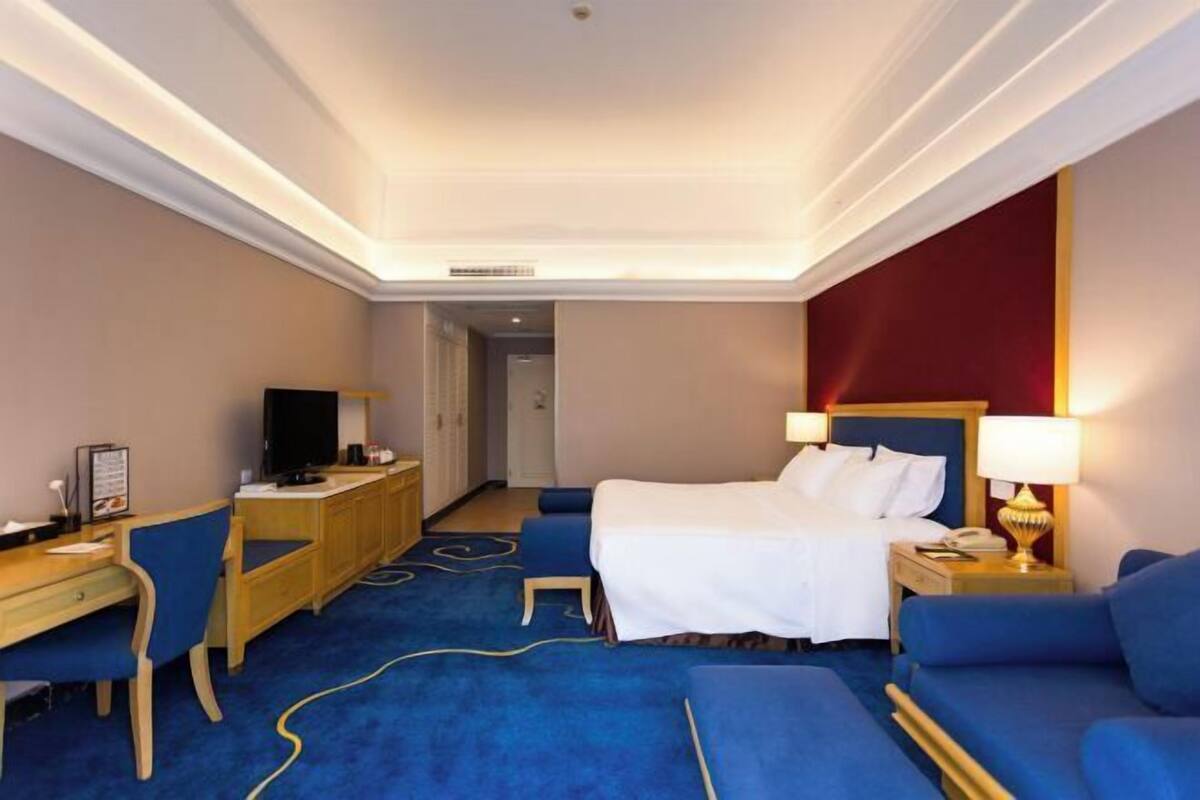 A hotel room with a bed, a desk, a chair, a TV, and a lamp.