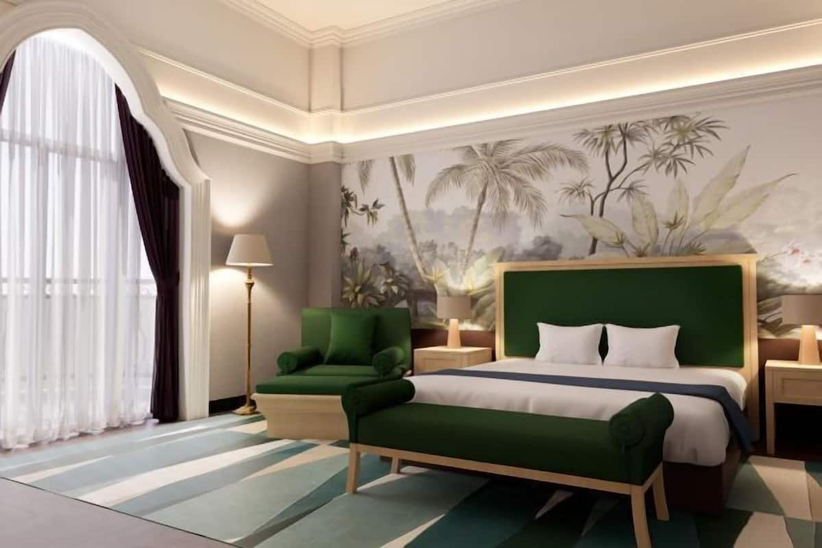 A hotel room with a large bed, green upholstered armchair, and a mural of tropical foliage on the wall.
