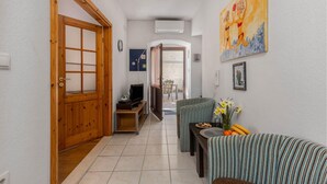 A hallway with a wooden door, a television, a dining area with striped chairs, and a painting on the wall.