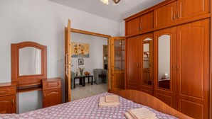A bedroom with a bed, wooden wardrobe, and a small table with a chair.