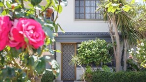 A building with a tiled roof, a gated entrance, and a well-maintained garden with various plants and a potted tree. - Studio Escape (Hamilton Hill)