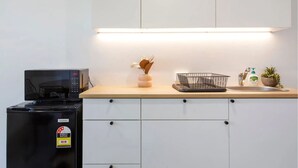 A kitchen with a microwave, a trash bin, a sink, and a countertop with a basket and a plant. - Studio Escape (Hamilton Hill)