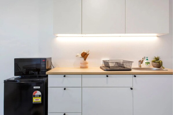 A kitchen with a microwave, a trash bin, a sink, and a countertop with a basket and a plant.