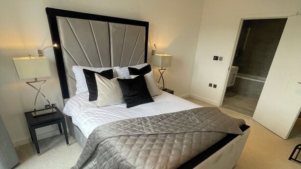 Een moderne slaapkamer met een groot bed, twee nachtkastjes met lampen, een garderobe en een schuifdeur naar een badkamer.