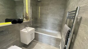 Een moderne badkamer met een glazen douchecabine, een witte wastafel en een ingebouwde handdoekhouder.