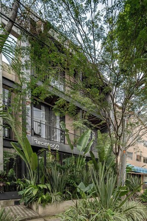 A building with balconies, surrounded by lush greenery and plants.