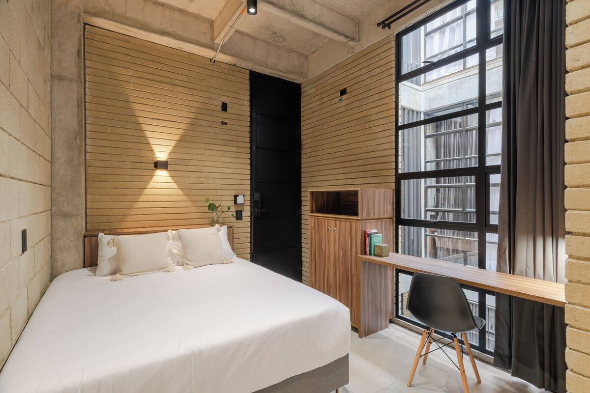 Une chambre moderne avec un grand lit, un bureau en bois et une fenêtre avec des rideaux.