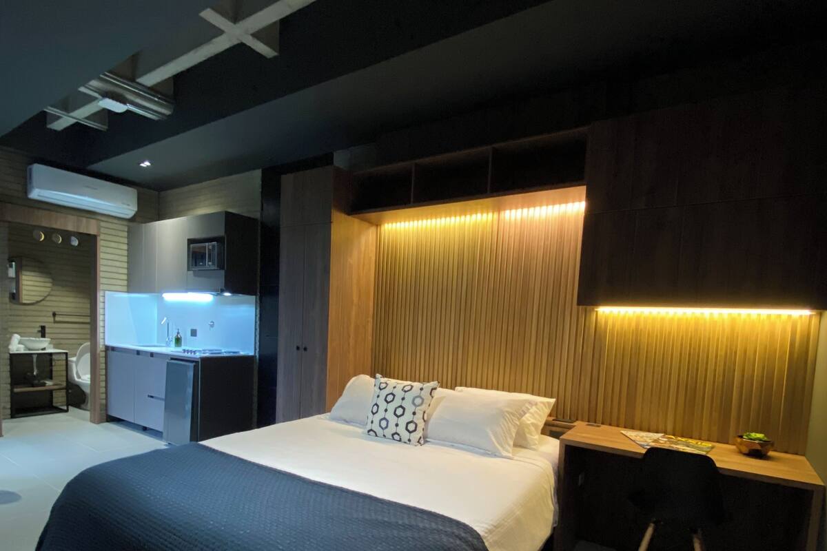 Une chambre d’hôtel moderne dotée d’un grand lit, de tables de chevet, d’un bureau et d’un coin cuisine intégré.