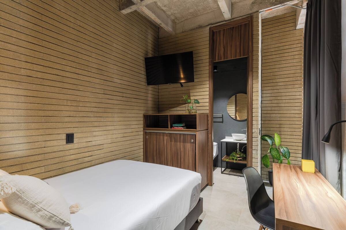 Une petite chambre comprenant un lit, un bureau, une télévision et un miroir.