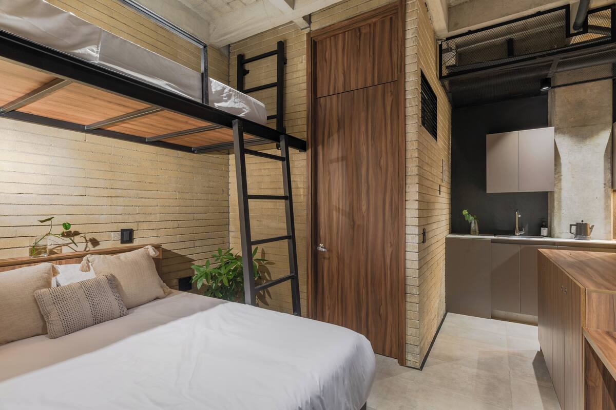 Une chambre à coucher de taille réduite, avec un lit superposé, une armoire en bois et un petit coin cuisine.