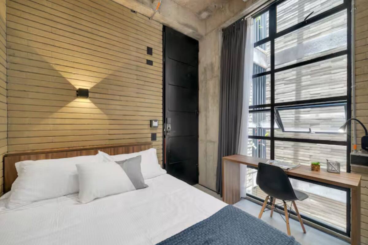 Une chambre d’hôtel moderne, dotée d’un grand lit, d’un bureau et d’une fenêtre offrant une vue sur la ville.