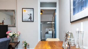 A dining area with a wooden table, chairs, a vase with flowers, a framed picture, and a mirror on the wall.