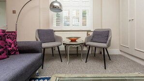 A living room with a sofa, two armchairs, a small round table, a floor lamp, and a window with shutters.