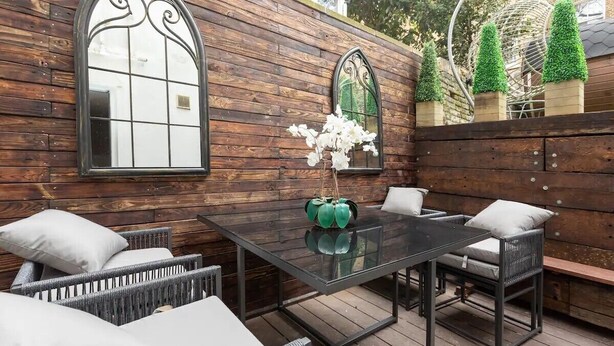 An outdoor patio with wicker furniture, a glass table, and decorative mirrors.