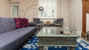 A living room with a sofa, two armchairs, a glass coffee table, a floor lamp, and a window with blinds.