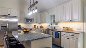 A modern kitchen with white cabinets, a stainless steel refrigerator, a granite countertop, and a hanging light fixture. - Cozy Acadia Hideaway with Hot Tub (Tremont)