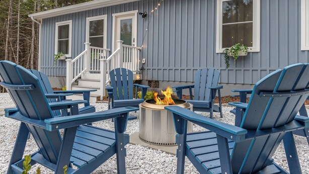 A blue house with a fire pit and four blue Adirondack chairs arranged around it. - Cozy Acadia Hideaway with Hot Tub (Tremont)