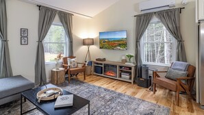 A cozy living room with a fireplace, comfortable seating, and a scenic view through the windows. - Cozy Acadia Hideaway with Hot Tub (Tremont)