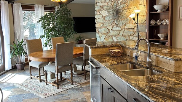 A kitchen with a stone accent wall, a dining area with a wooden table and chairs, and a built-in island with a sink.