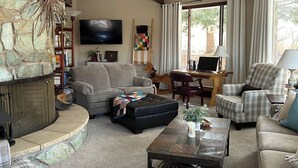 A living room with a stone accent wall, a fireplace, a television, and a view of the outdoors through large windows.