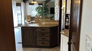A kitchen with a large island, dark wooden cabinets, and a stone backsplash. There is a ceiling fan and pendant lighting above the island.