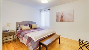 Une chambre à coucher avec un lit, une table de chevet, une lampe, un banc et un tableau au mur.
