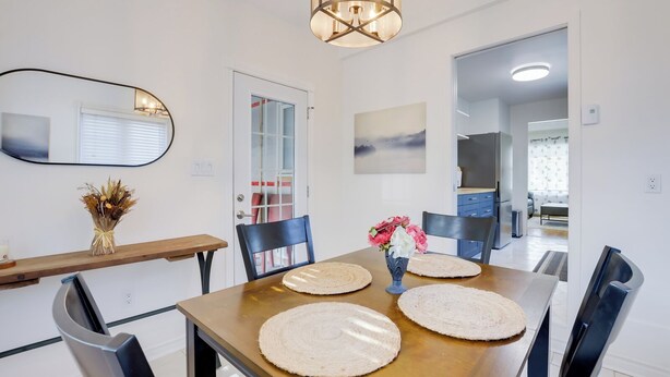 Un coin repas avec une table en bois, quatre chaises, un vase de fleurs et un miroir au mur.