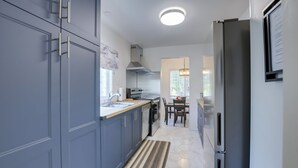 Une cuisine moderne avec des meubles gris, un réfrigérateur en acier inoxydable et un coin repas comprenant une table et des chaises.