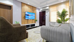A modern living room with a flat-screen TV, wooden panel wall, and a large potted plant.